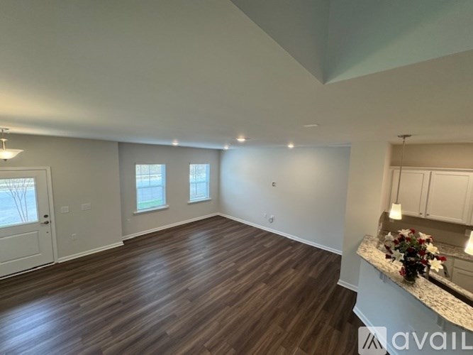A spacious room with wood flooring and a kitchen area with white cabinets.