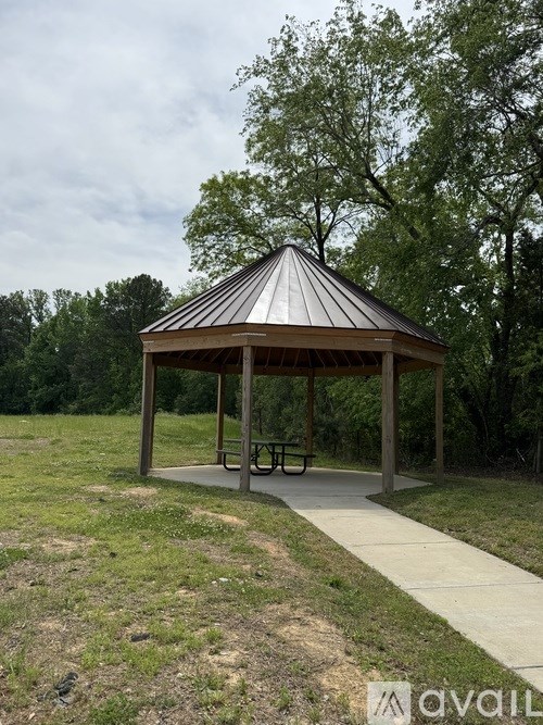 A gazebo in a park with a picnic table and a concrete walkway.