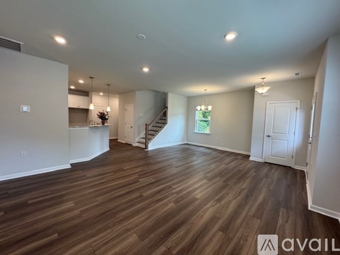 A spacious room with wooden flooring and a staircase in the background.