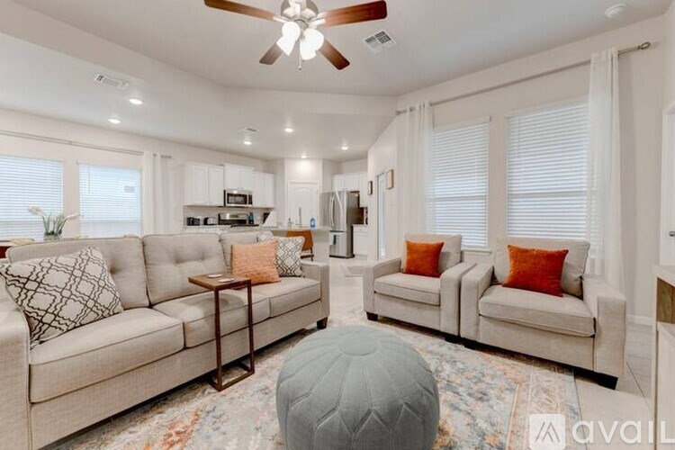 A living room with a beige sofa, a grey ottoman, and a ceiling fan.