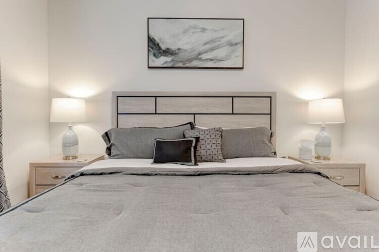 A bedroom with a large bed, two nightstands with lamps, and a framed picture on the wall.