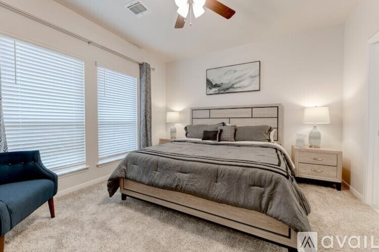 A bedroom with a large bed, a blue chair, and a ceiling fan.