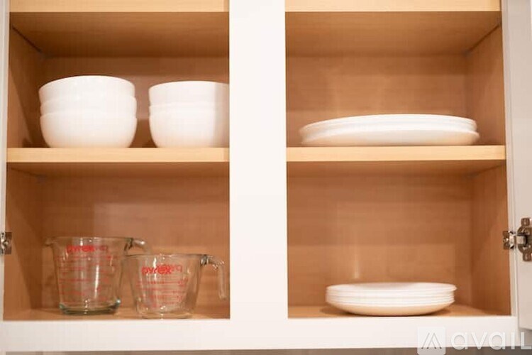 A kitchen cabinet with two shelves, one with two bowls and the other with a plate and two measuring cups.