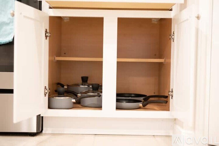 A white cabinet with two shelves is open, revealing several pots and pans.