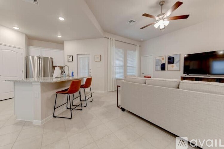 A kitchen with white cabinets and a refrigerator, a dining table with chairs, and a living room with a couch and a television.
