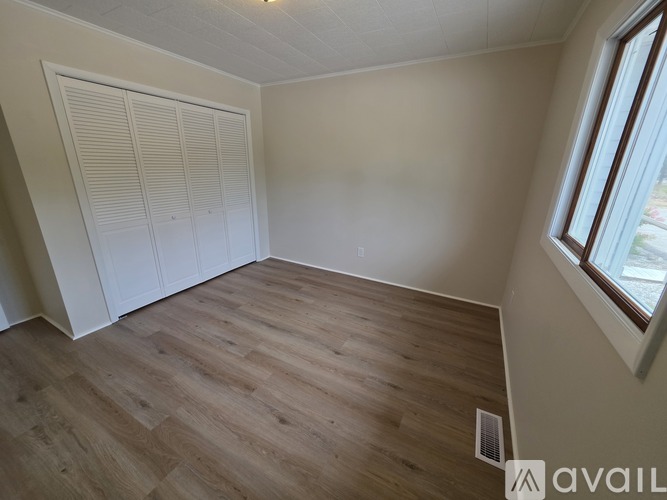 A room with wooden flooring and a window on the right side.