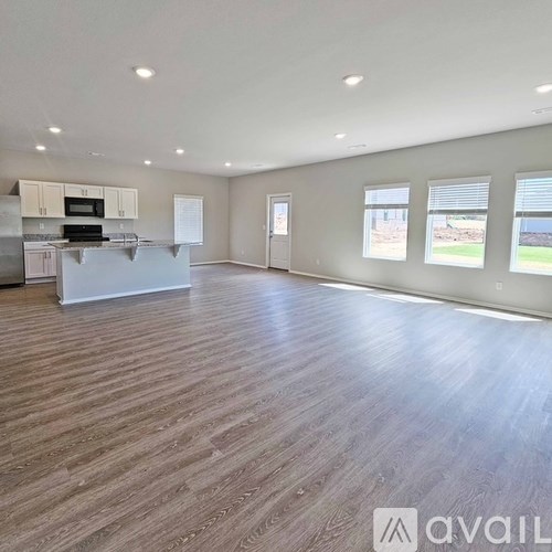A spacious room with wooden flooring and a kitchen area with white cabinets and appliances.
