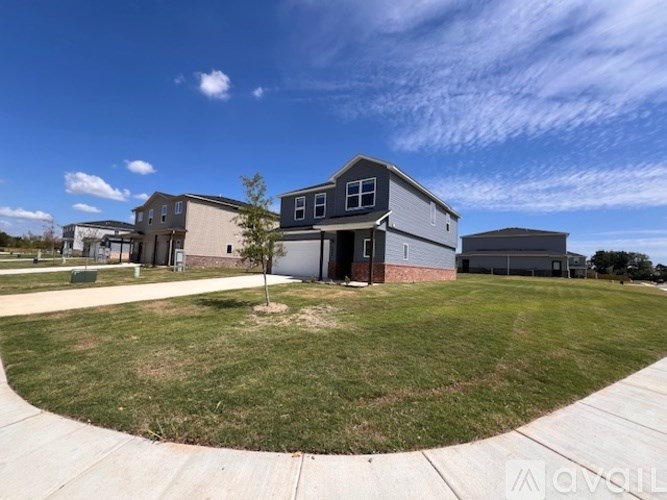 A small tree stands in a grassy circle in front of a grey house.