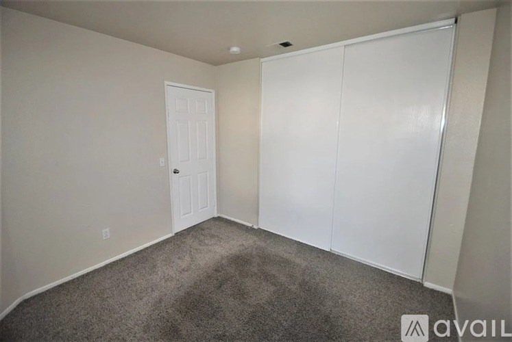 A room with a carpeted floor, a white door, and a white closet.