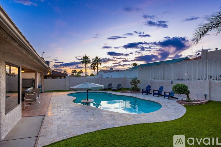 A pool surrounded by a patio and lawn with a sunset in the background.