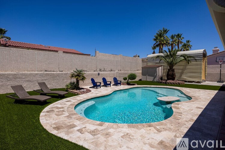 A pool surrounded by a concrete border and a lawn with chairs.