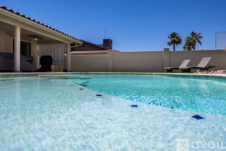 A pool in a backyard with a house and palm trees in the background.