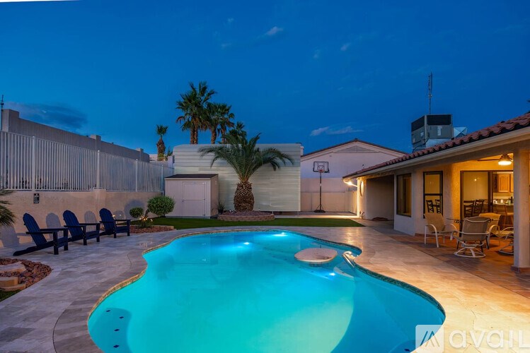 A pool in a backyard at night with lights on.