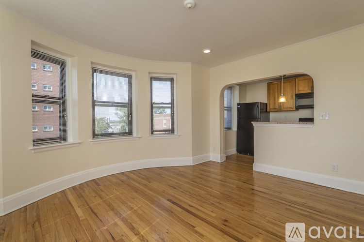 A room with wooden floors and a kitchen area in the background.