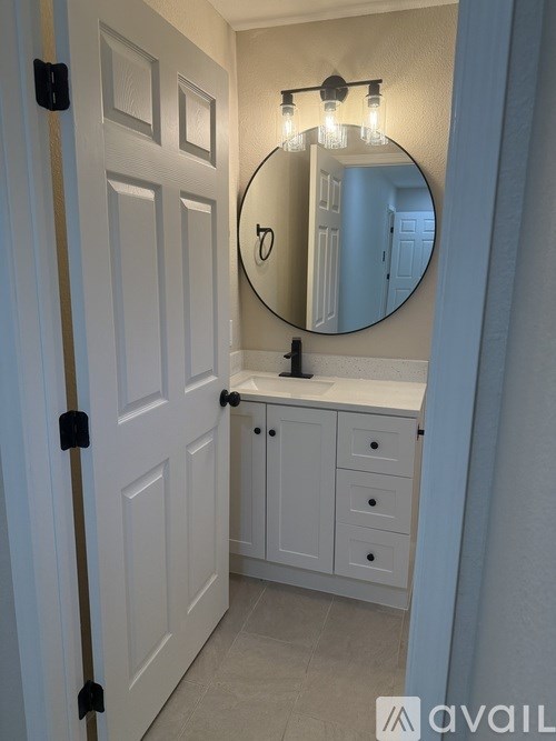 A bathroom with a white door, a round mirror, and a cabinet with drawers.