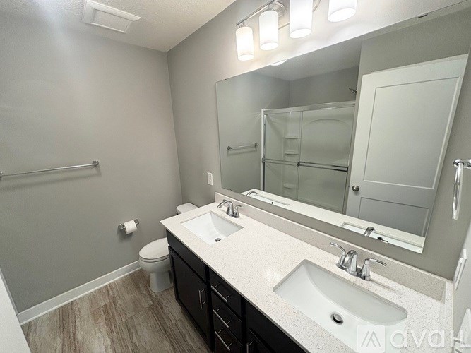 A bathroom with a toilet, sink, mirror, and lighting fixture.