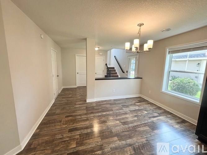 A living room with wood flooring and a staircase in the background.