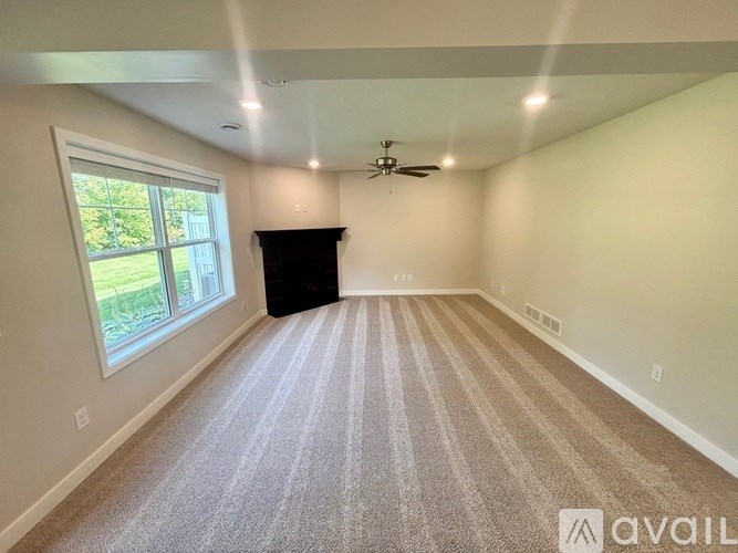 A spacious room with a carpeted floor, a ceiling fan, and a large window with a view of greenery outside.