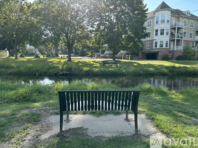 A park bench sits in front of a pond with a building in the background.