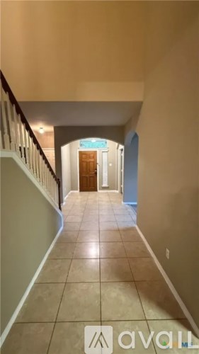 A hallway with a tiled floor and a staircase with a railing.