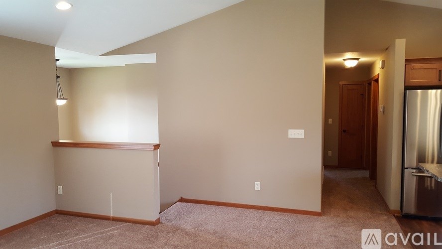 A spacious room with beige walls and carpeted floor, featuring a kitchenette with a stainless steel refrigerator.