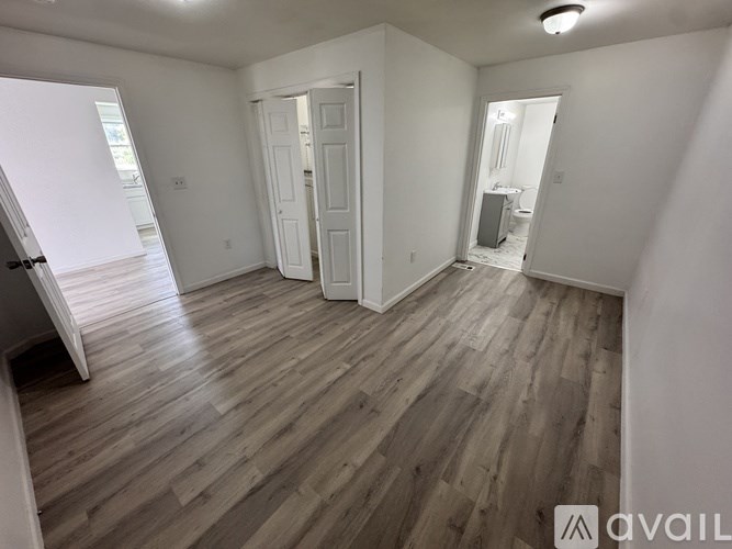 A room with wooden flooring and white walls, with a doorway leading to another room.