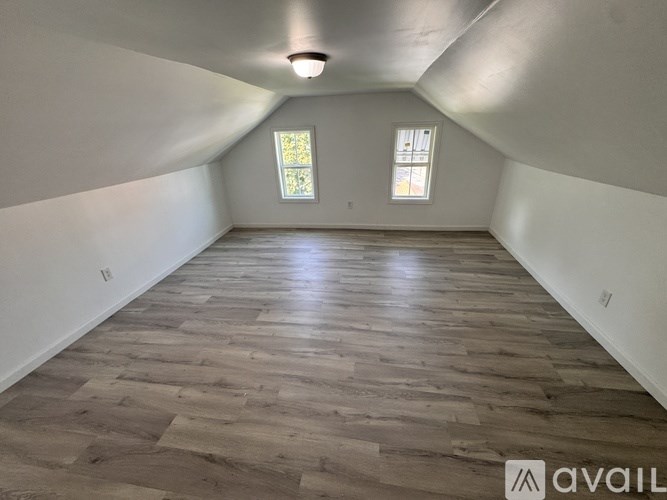 A room with wooden flooring and two windows.