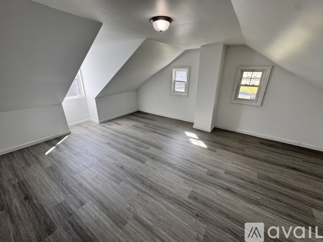 A room with wooden flooring and two windows.