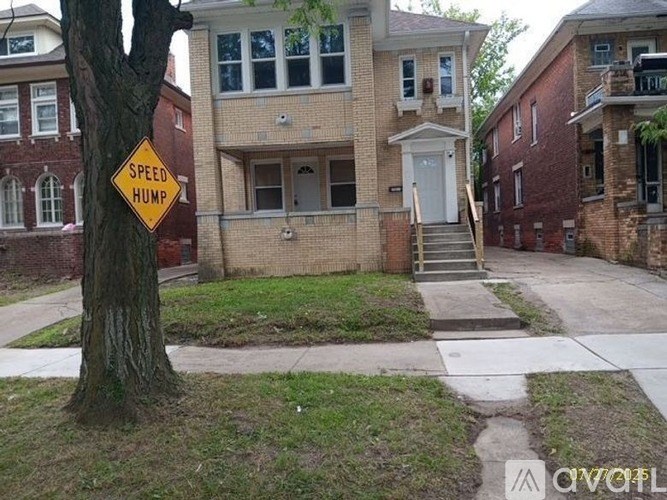 A speed hump sign is in front of a tree and a house.