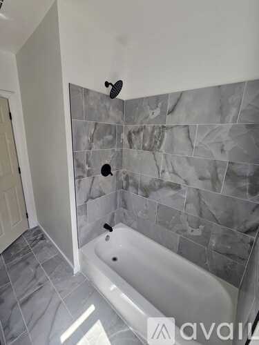 A bathroom with a tub and grey tiles.