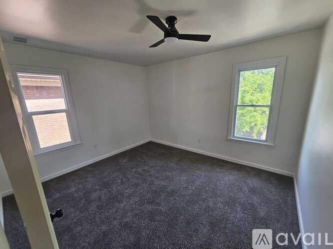 A room with a ceiling fan and two windows.