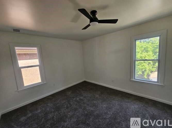 A room with a ceiling fan and two windows.