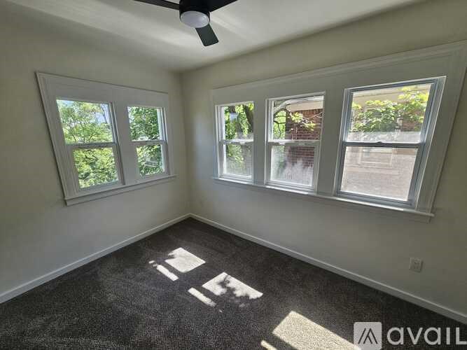 A room with a carpet floor, a ceiling fan, and three windows.