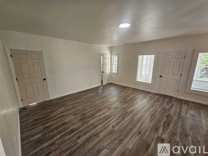A room with wooden flooring and white walls, with a window on the right side.