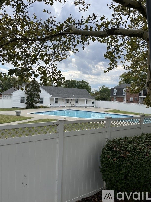 A pool surrounded by a white fence with trees in the background.
