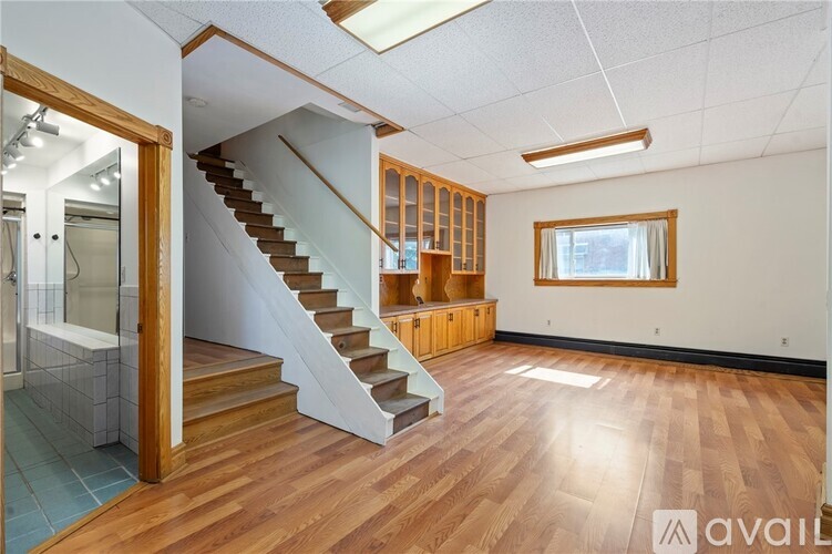 A spacious room with wooden flooring and a staircase leading to another level.