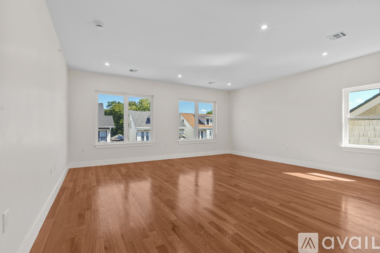 A spacious room with wooden flooring and two windows.