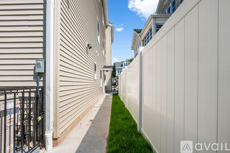A narrow alley with a white fence on the right and a building with a window and air conditioner on the left.