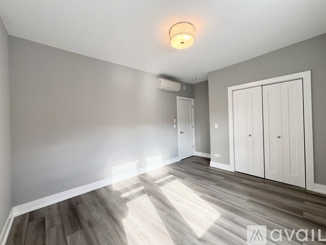 A room with a wooden floor and white walls, with a light on the ceiling and a window with blinds.