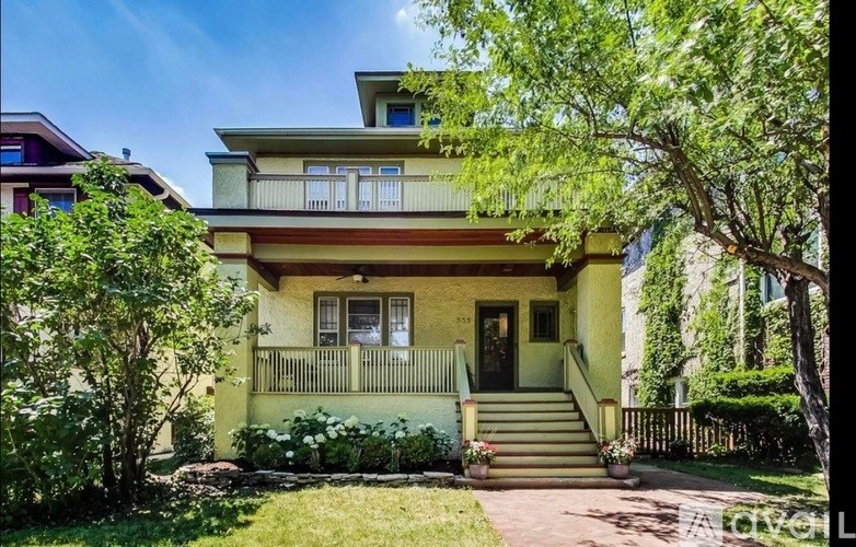 A yellow house with a balcony and a staircase leading to the front door.