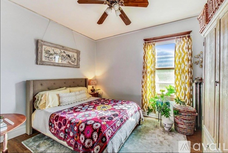 A bedroom with a bed, a ceiling fan, and a window with yellow curtains.