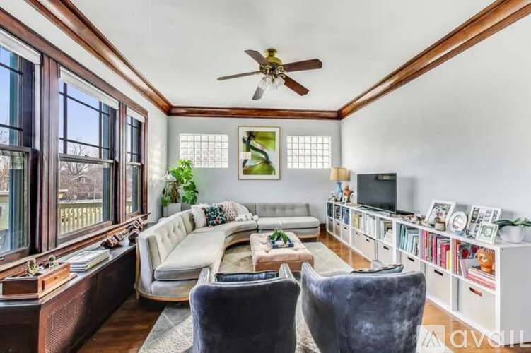 A living room with a white couch, a grey chair, a wooden table, and a ceiling fan.