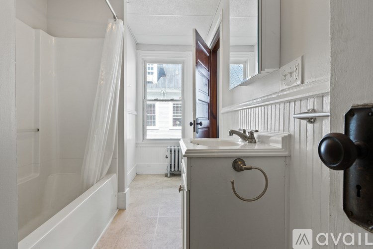 A bathroom with a white tub, sink, and a window with a view of buildings outside.