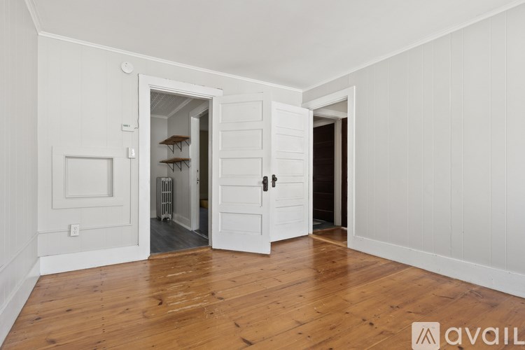 A room with white walls and wooden floors has two open doors.
