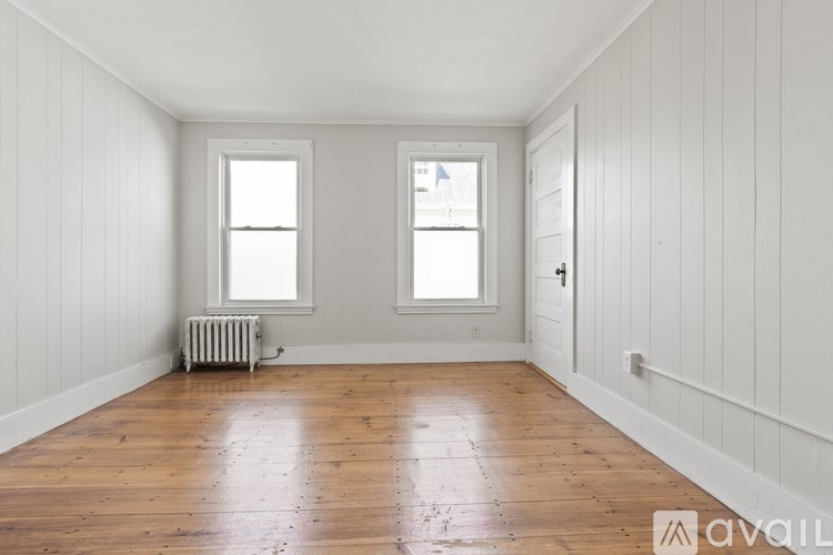 A room with wooden floors and white walls with two windows.