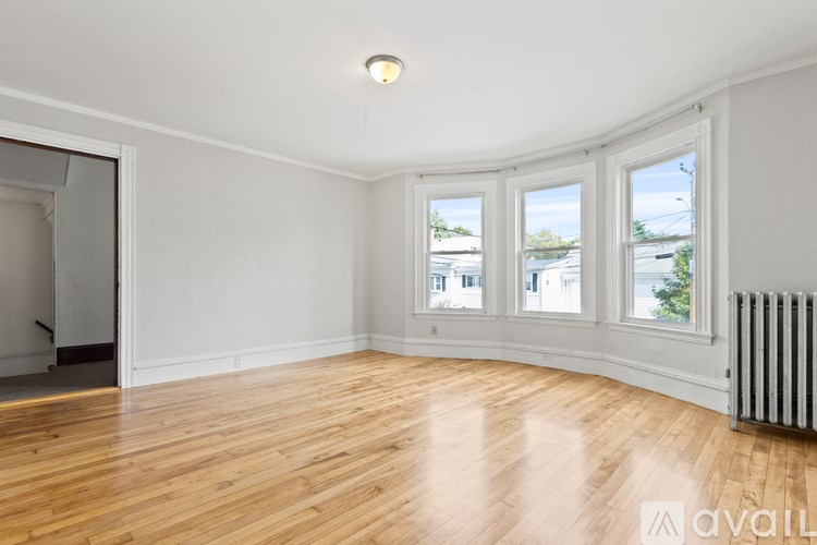 A room with wooden floors and white walls, with a window showing a view of a street and houses.
