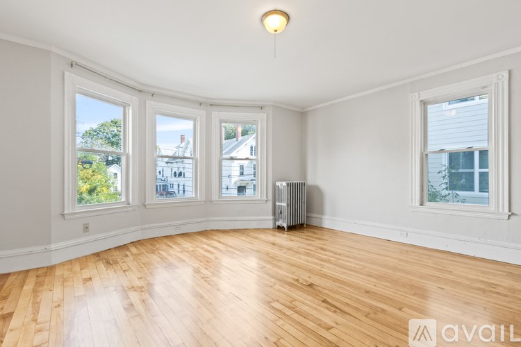 A room with wooden floors and white walls has a window with a view of a house.