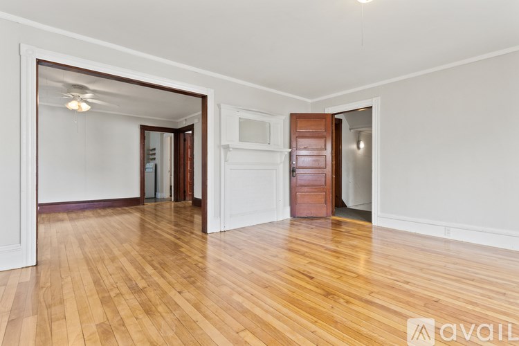 A room with wooden floors and white walls, with a door on the right and a mirror on the left.