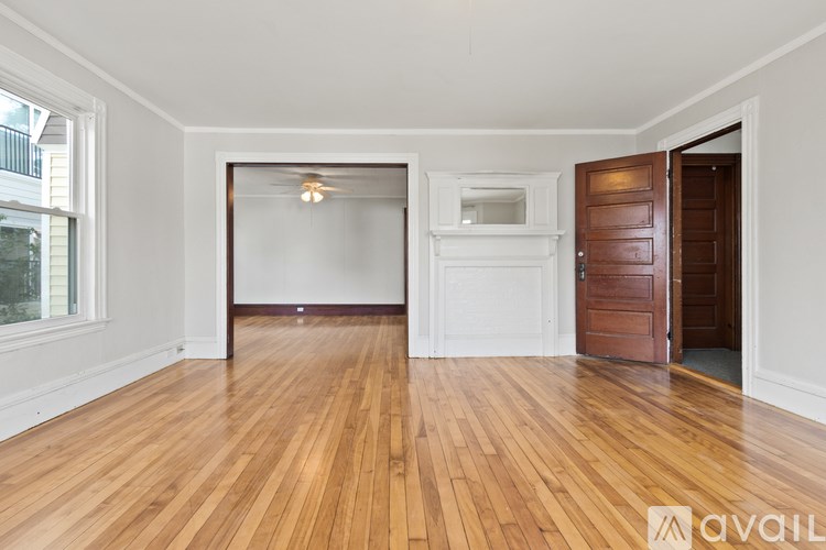 A room with wooden floors and white walls, with a window on the left and a door on the right.
