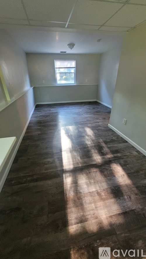 A room with wooden flooring and a window letting in sunlight.
